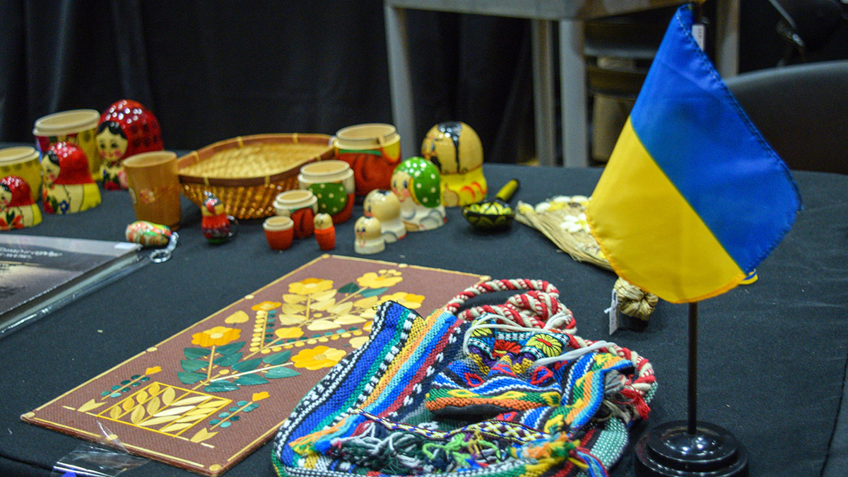 A stand with the Ukrainian flag, as well as a bag decorated with embroidery, nesting dolls and an art piece depicting a pattern of yellow flowers.  