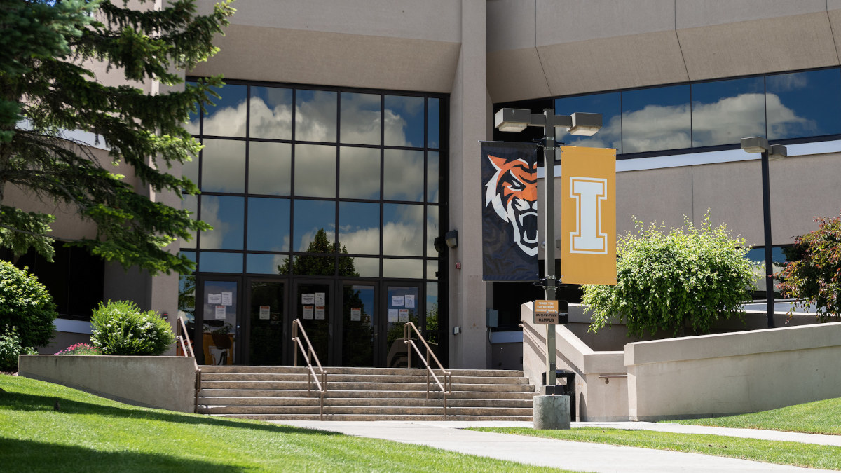A white block I on a gold banner hangs outdoors on a sunny day at the Idaho Falls campus.