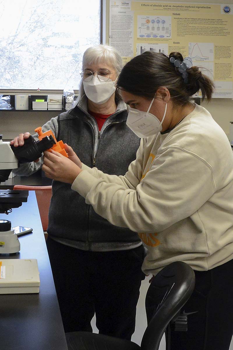 Two women inspect a microscope in a lab.