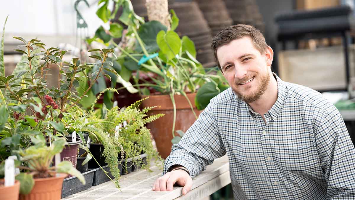 A person leaning on a table with plants in pots.