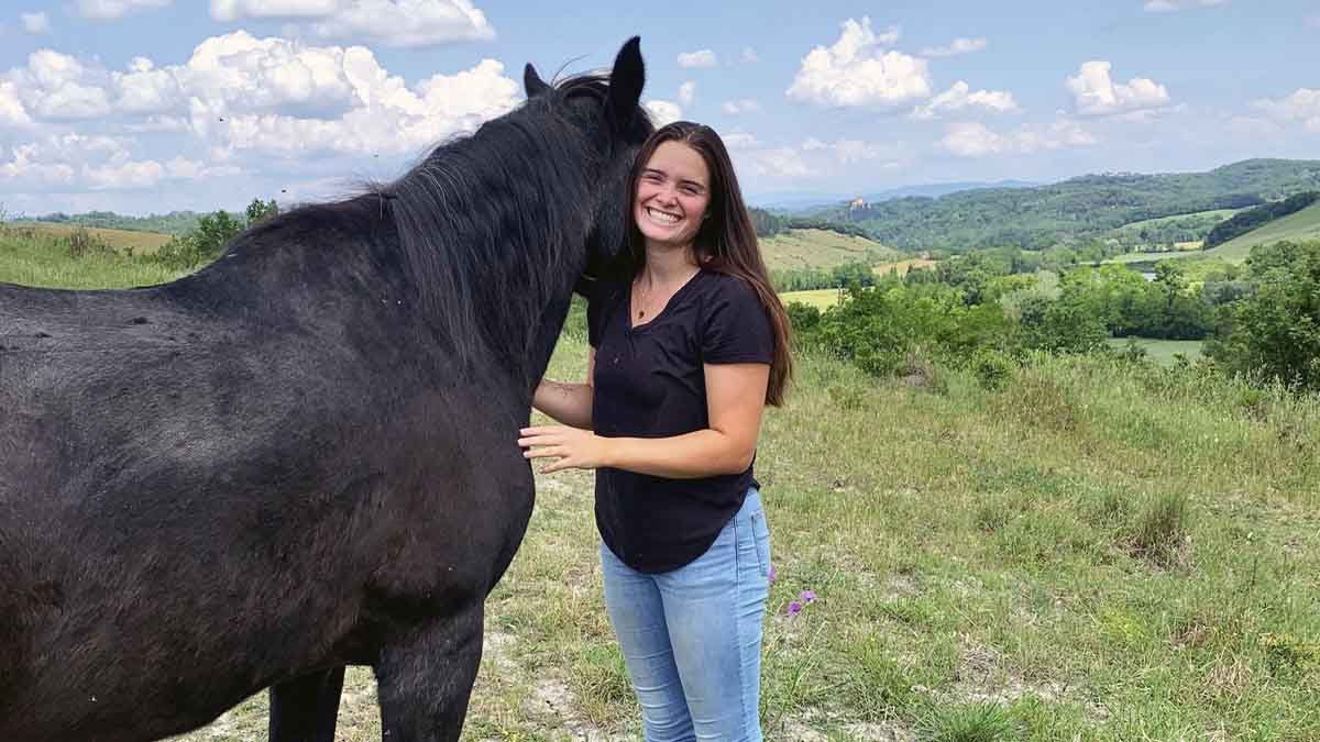 A woman stands next to a horse in the Italian countryside.