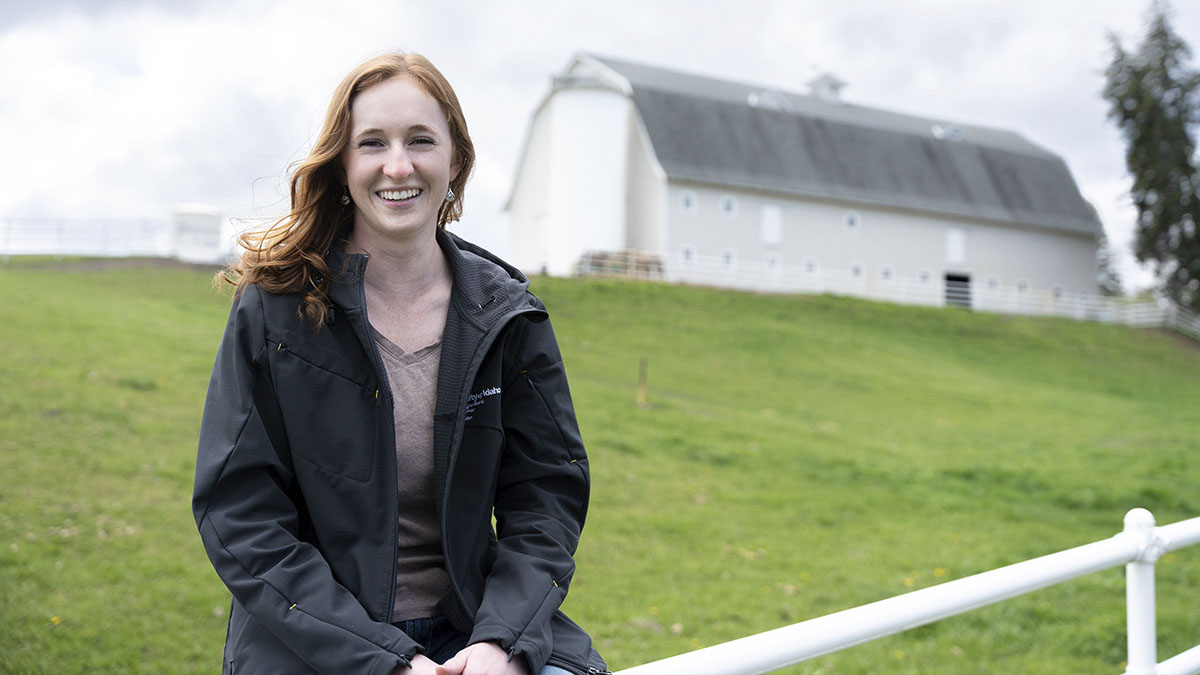 A person sitting on a white fence with a white barn in the background.