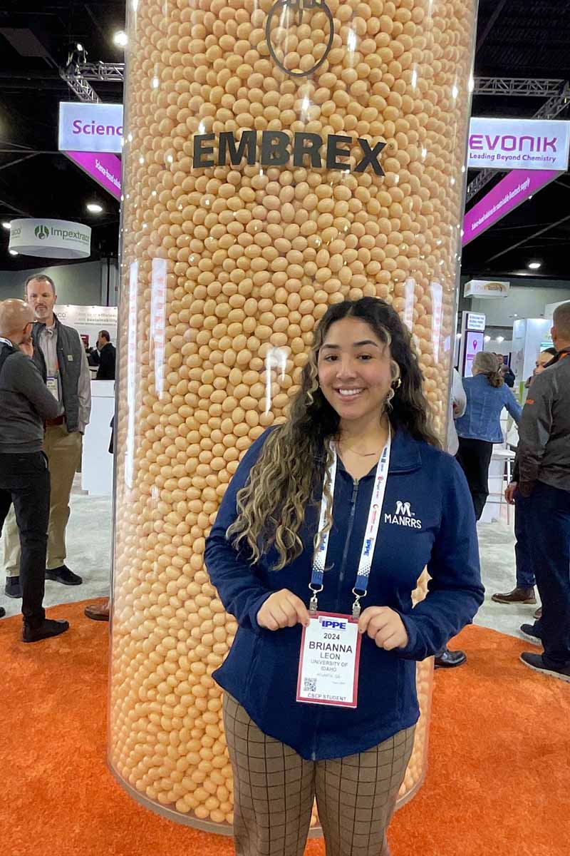 A young woman poses in front of a large column of eggs at a professional conference. 