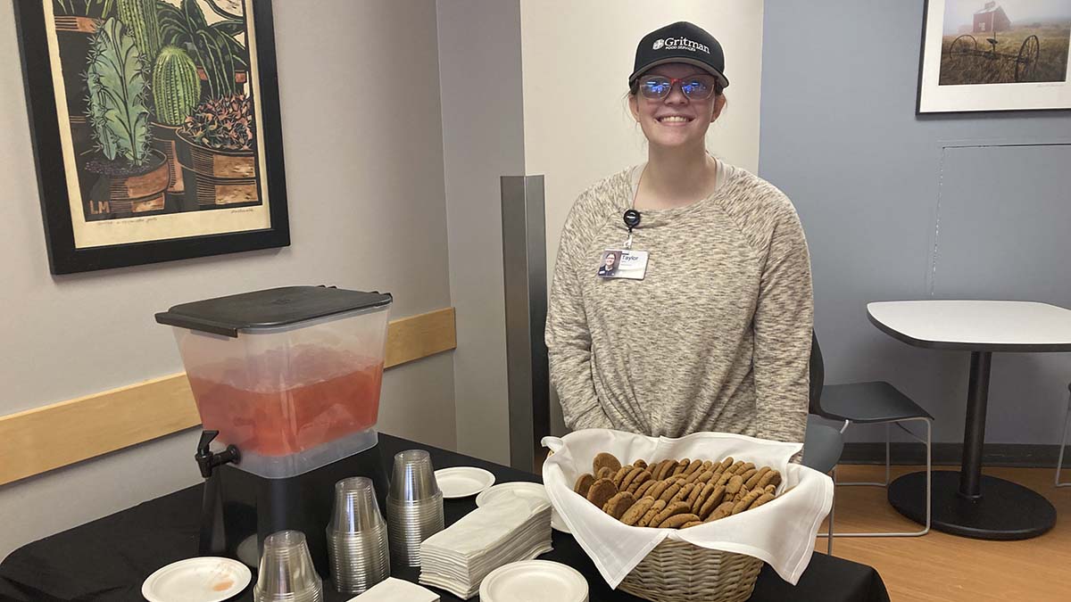 A woman standing behind a table with cookies and punch.