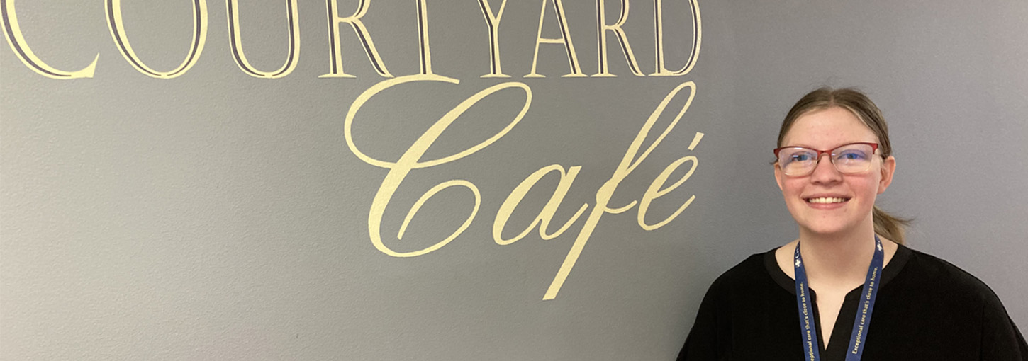 Portrait of a woman standing in front of a courtyard cafe sign.