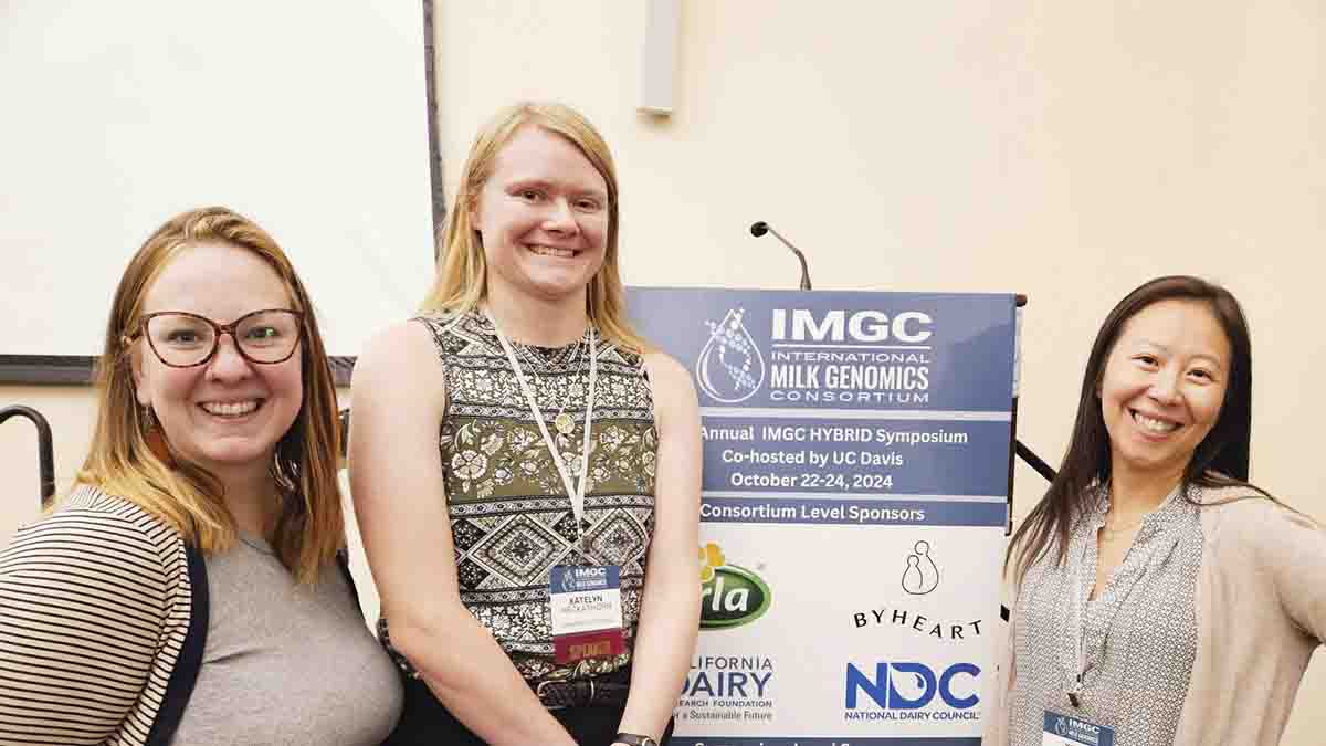 Three women standing in front of a conference sign.