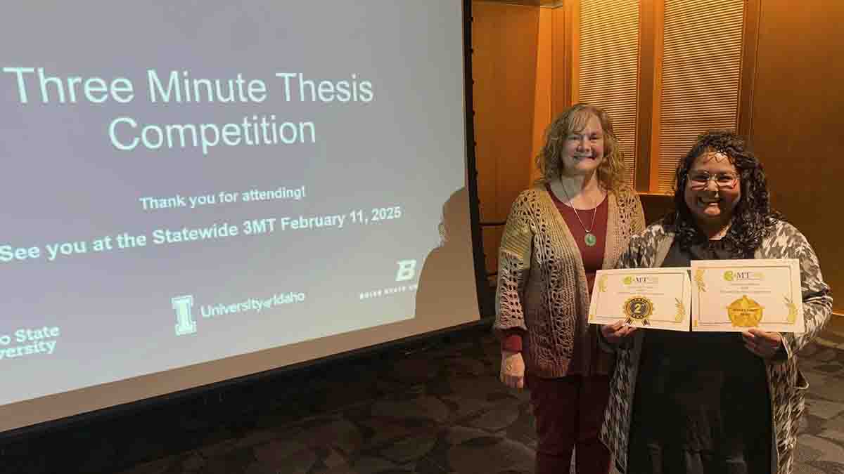 Two women next to a screen, one holding two certificates.