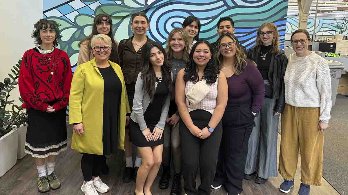 A group photo in front of a swirly design of artwork.