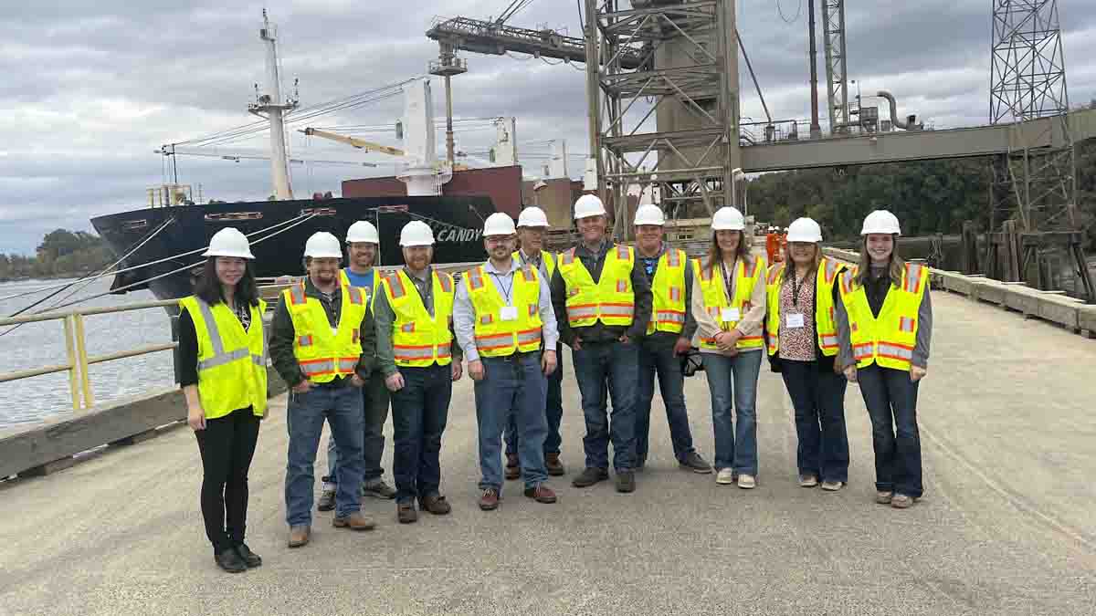 A group of men and women wearing hard hats standing on a ship dock.