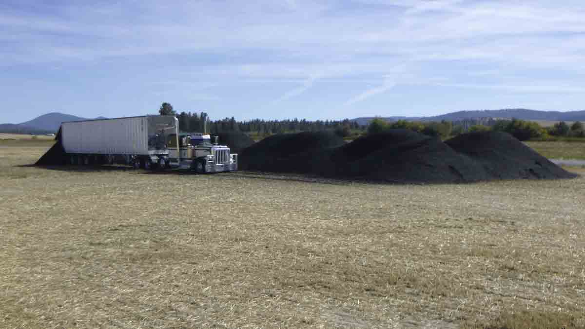 A semi out in a fields next to a pile of dirt.