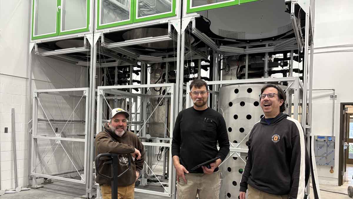 Three men in a building with ecotron equipment.