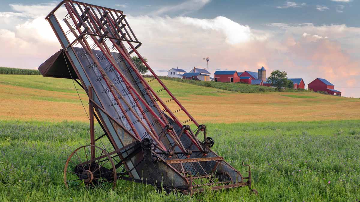 An old thresher in a field with a family farm in the background