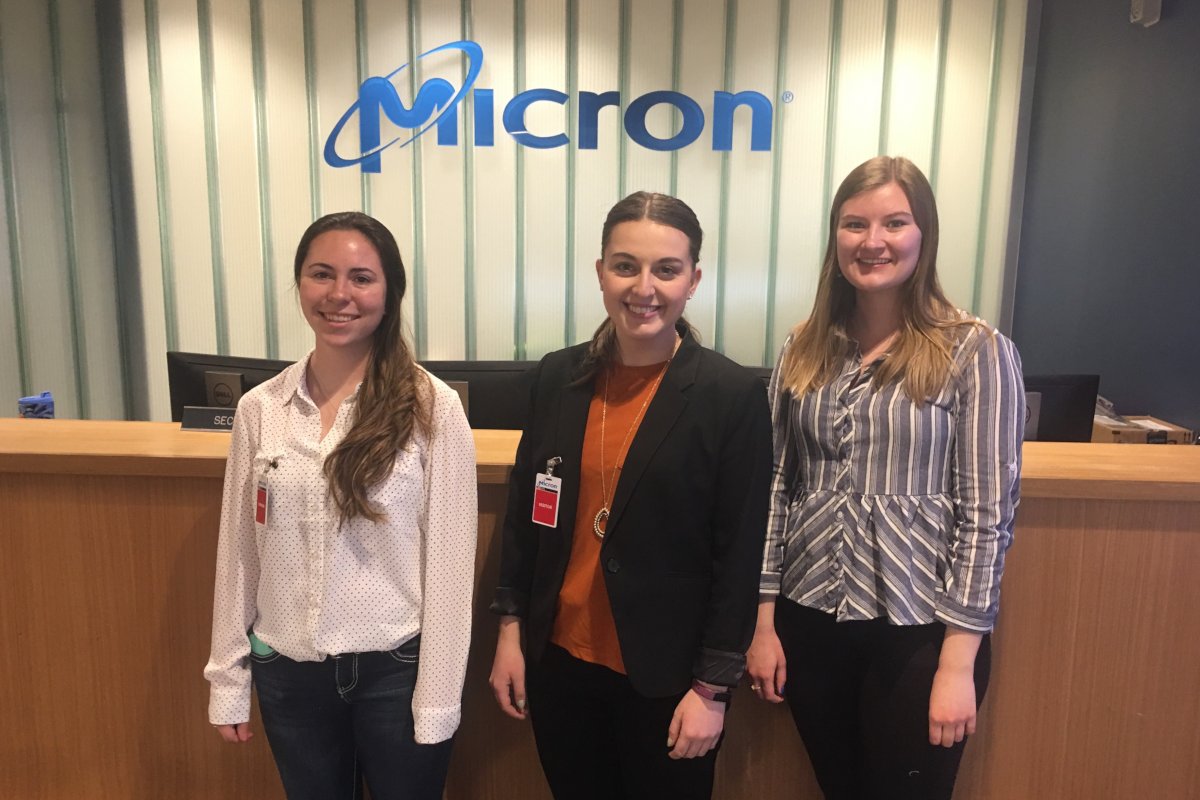 Morgan Hughes, Hayley Parks and Kaarin Von Bargen stand in front of a Micron logo mounted on the wall.