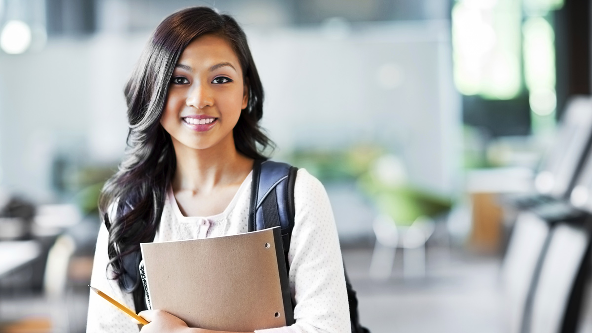 A student stands ready with her notebook and pencil in hand.