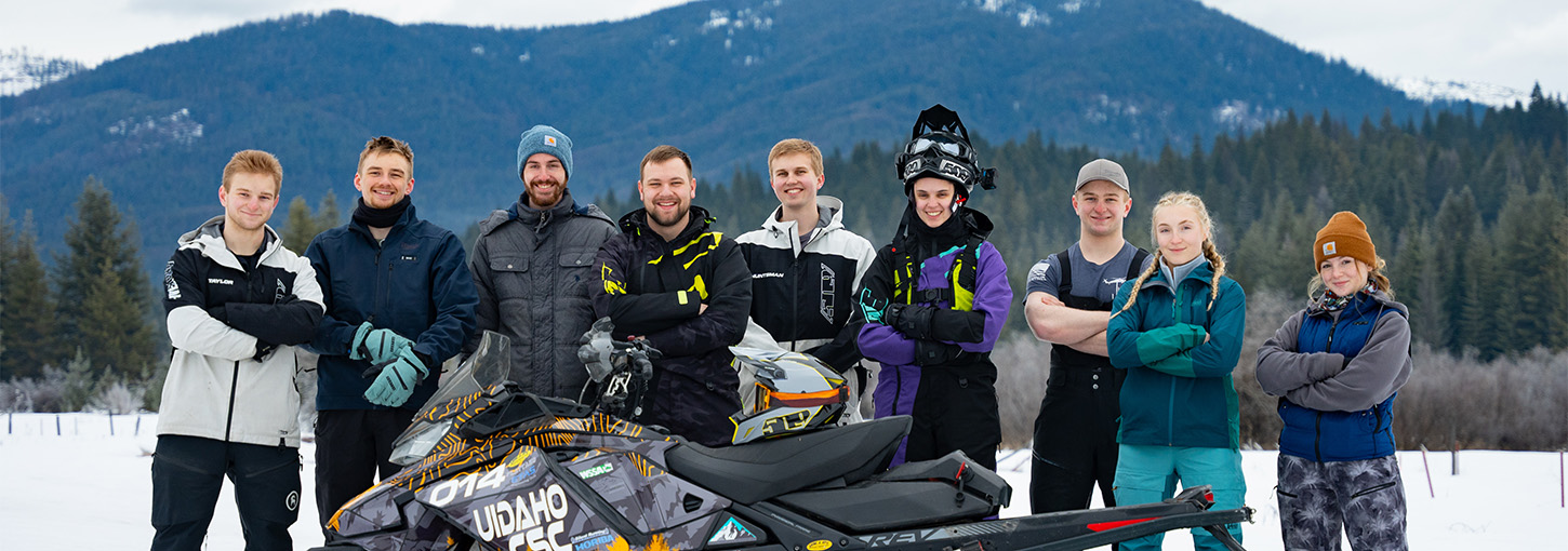 Students standing in a field of snow behind a snowmobile
