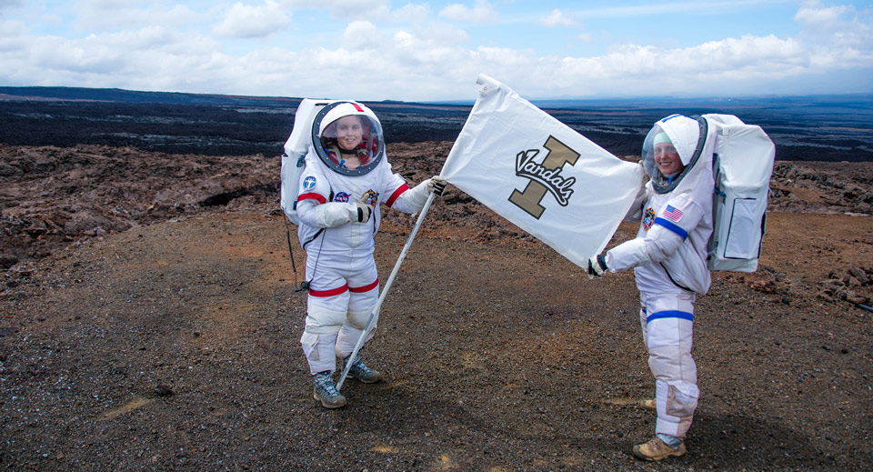 Sophie Milam holds a UI Vandals Flag while wearing the prototype space suit.