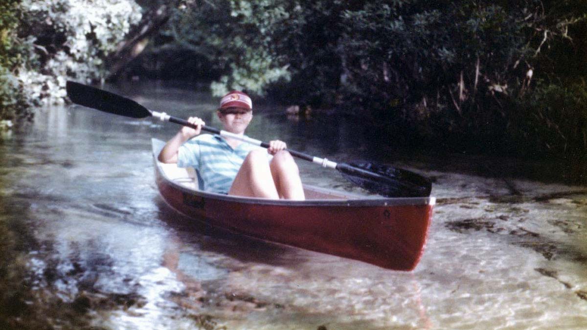 A young Jim Ekins looks at the camera while rowing a canoe down a river in Florida.