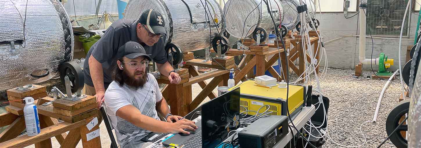 Two men look at a computer in a room with dairy manure composters.