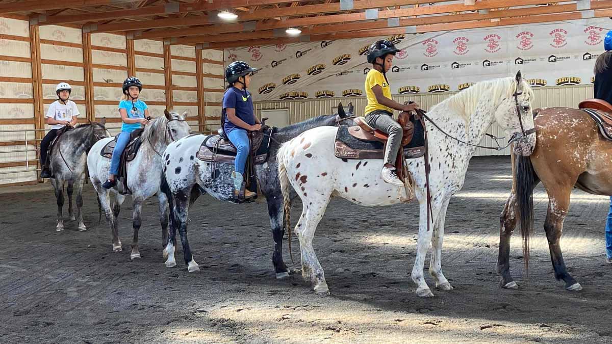 Several youth ride horses indoors.