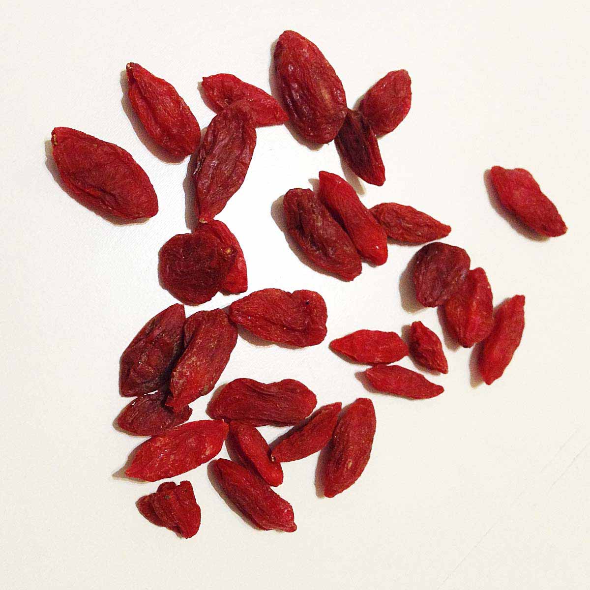 Dried goji berries laid out on white surface.