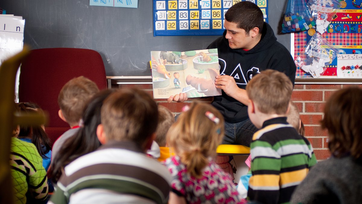 Education student reads a story to a group of young students.