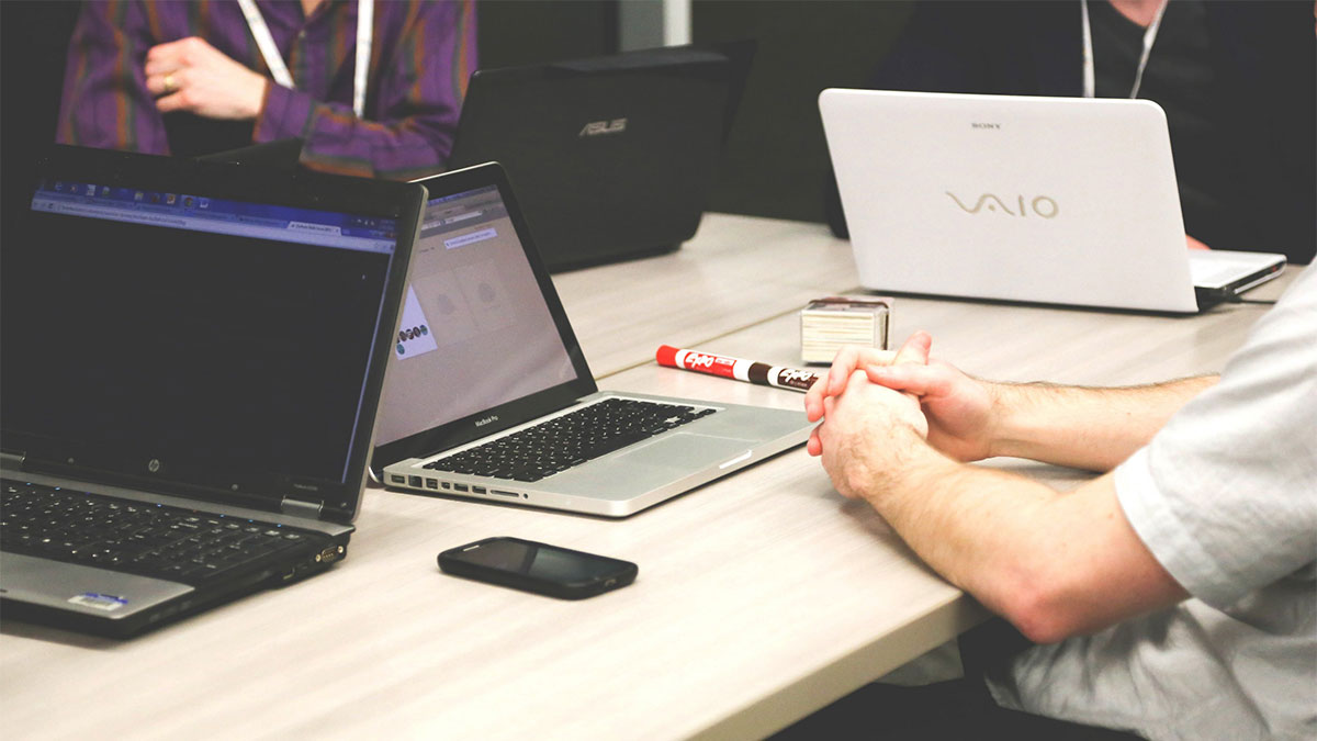 People meet with laptops on small table.