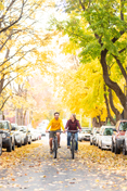 Two students ride down Greek Row in the fall, amid changing leaves.