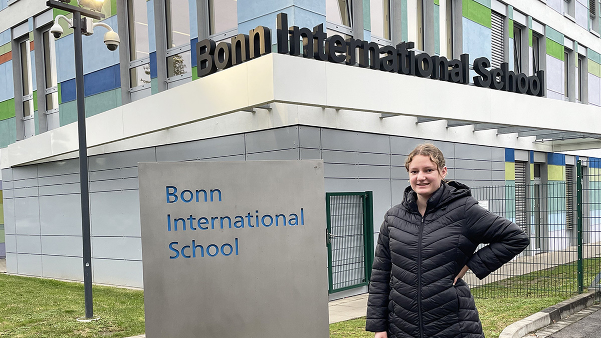 Woman standing in front of Bonn International School sign.
