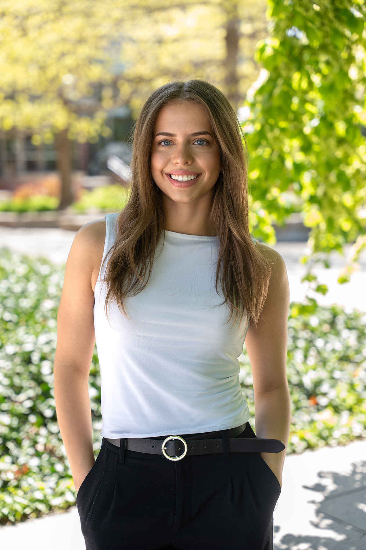 A woman in a white shirt stands in the shade of a tree.