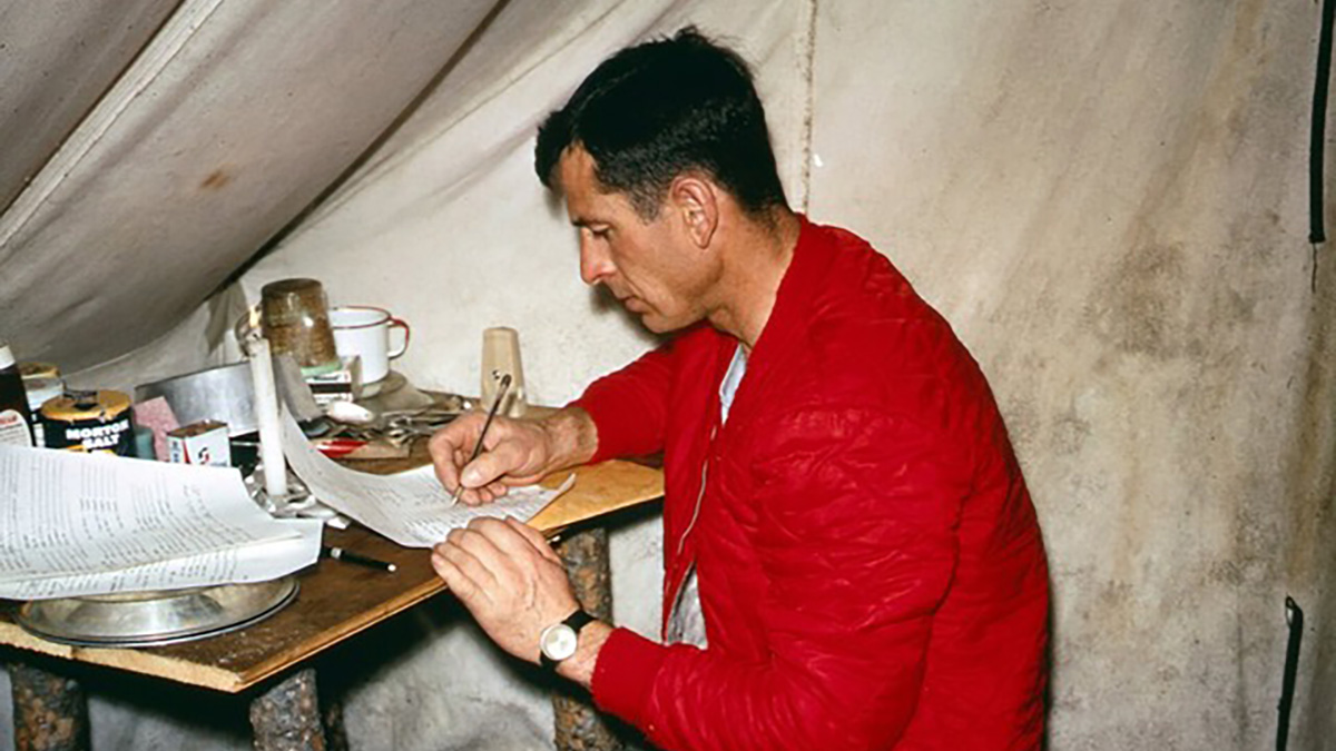 A man sits in a tent and writes in a notebook.