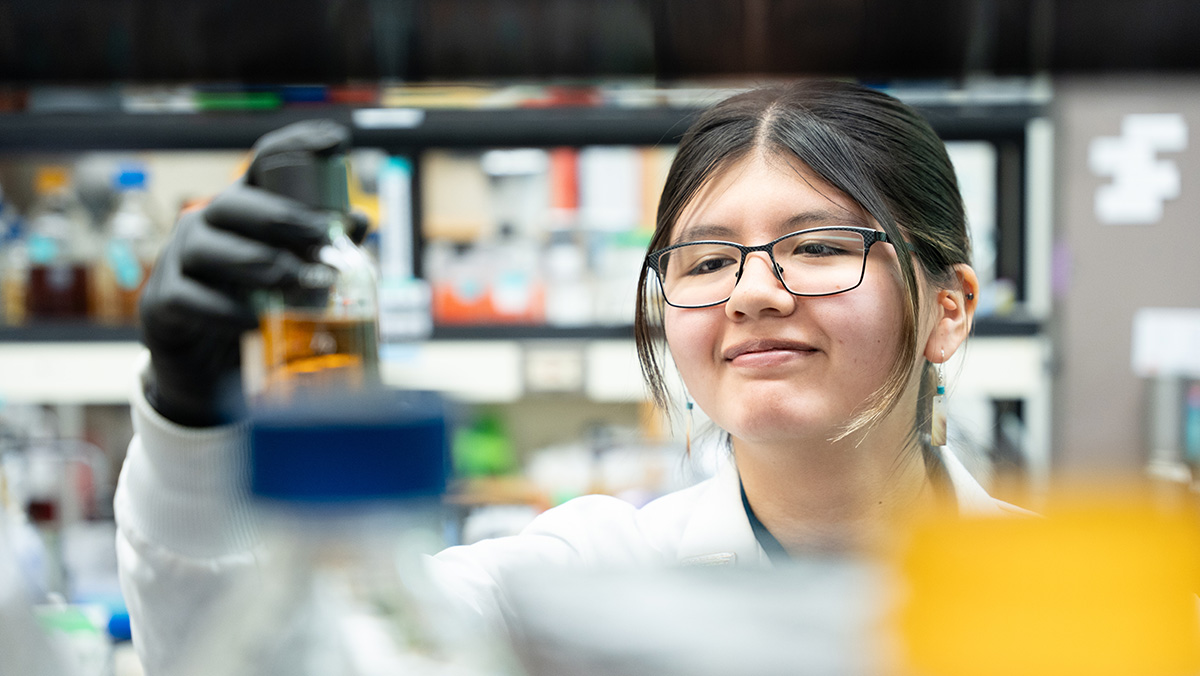 Smiling woman with glasses peers at a raised Petri dish.