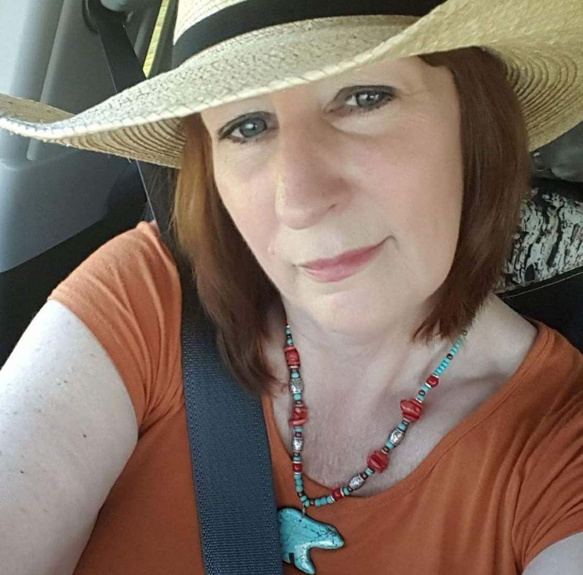 Closeup of woman wearing hat and orange top.