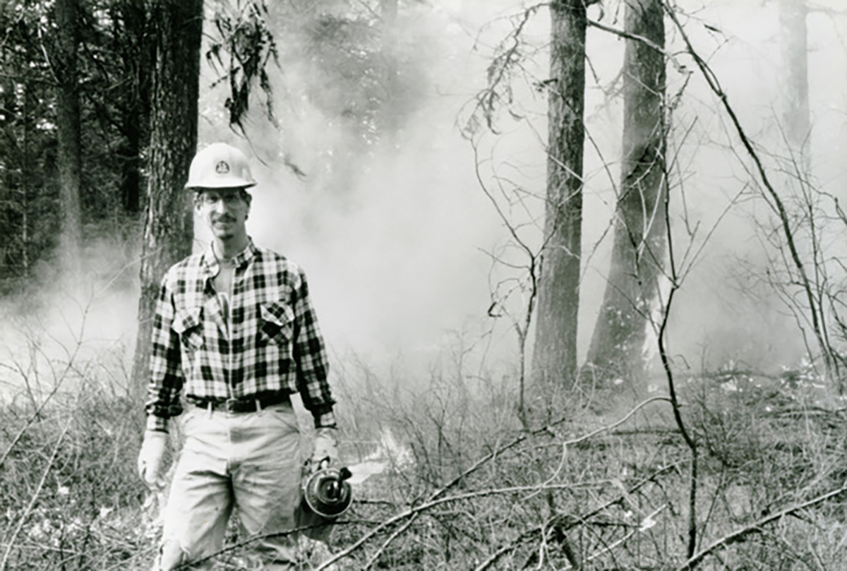 A man stands in front of a ground fire.