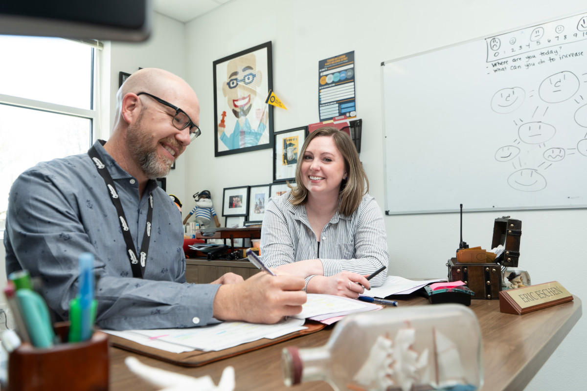 Woman and man sitting behind desk smiling and looking into the camera.