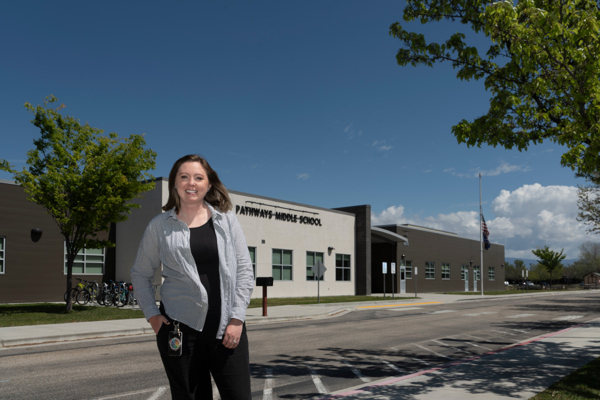 Woman standing in front of a middle school smiling and looking at the camera.