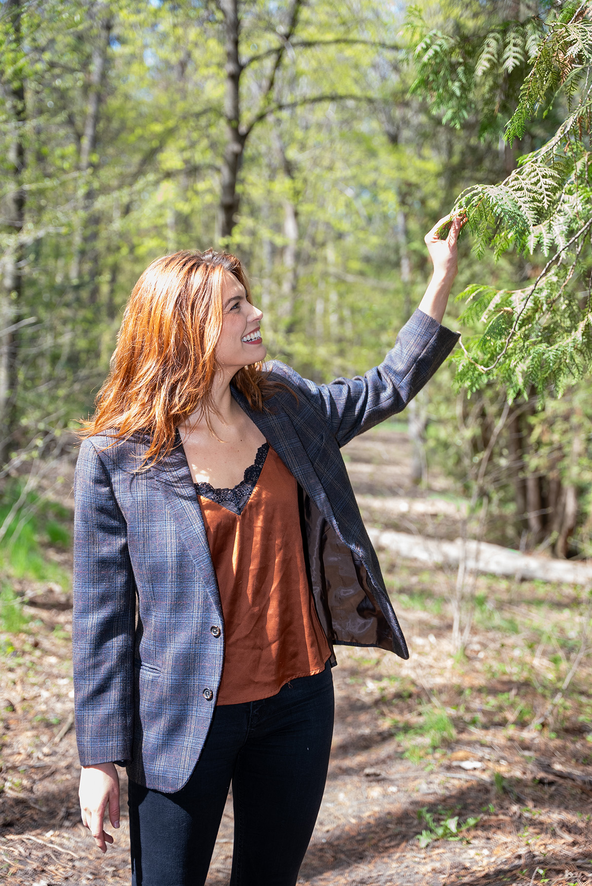 Woman on a park trail reaches up for a tree branch.