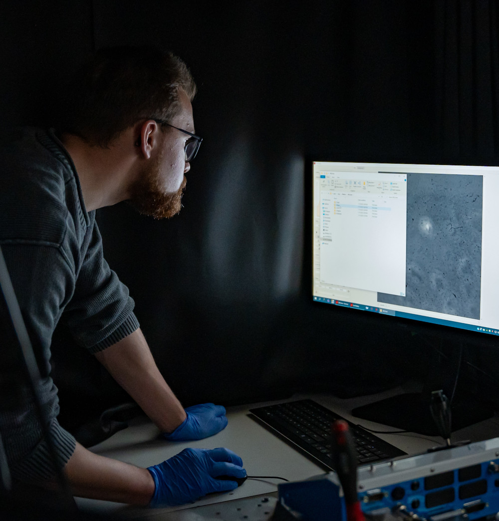 Bearded student wearing spectacles examining magnified cells on screen