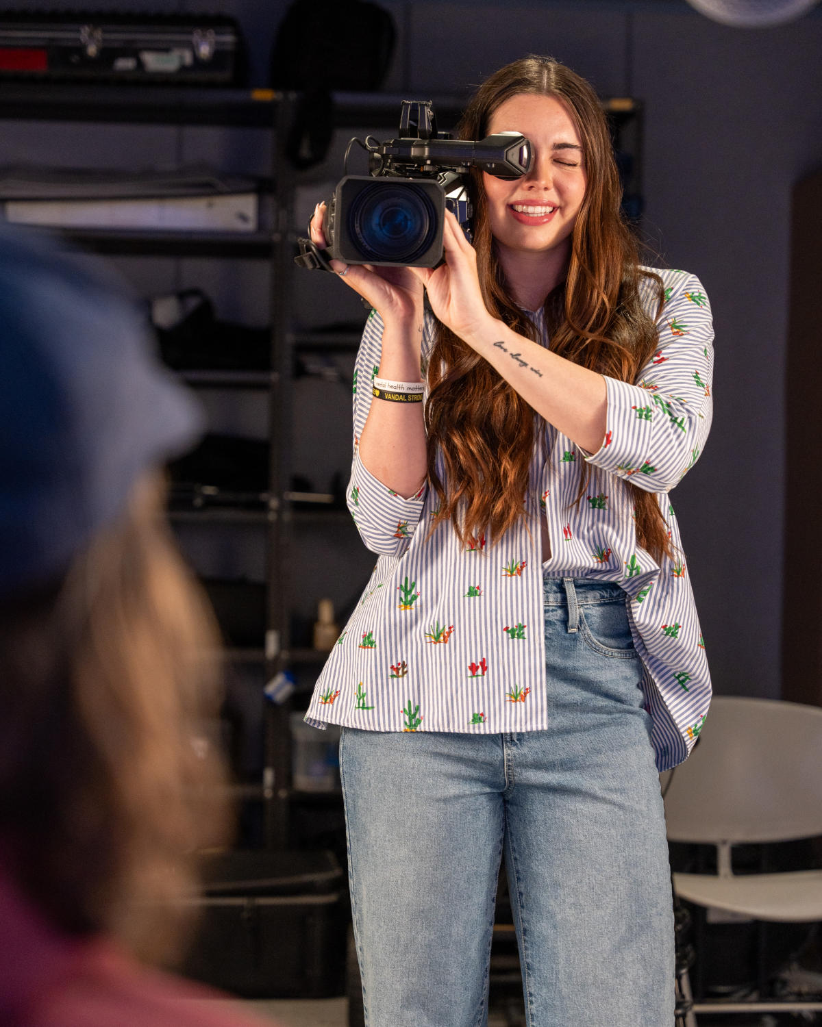 Woman stands in film studio looking through a film camera.