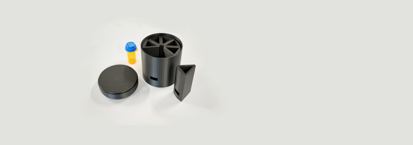Photo of three dispenser components and an empty pill bottle on a white table.