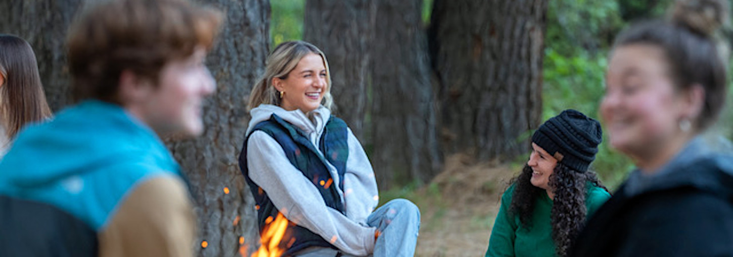 A woman sits by a campfire.