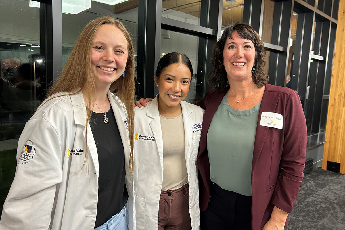 Three women standing together and smiling.