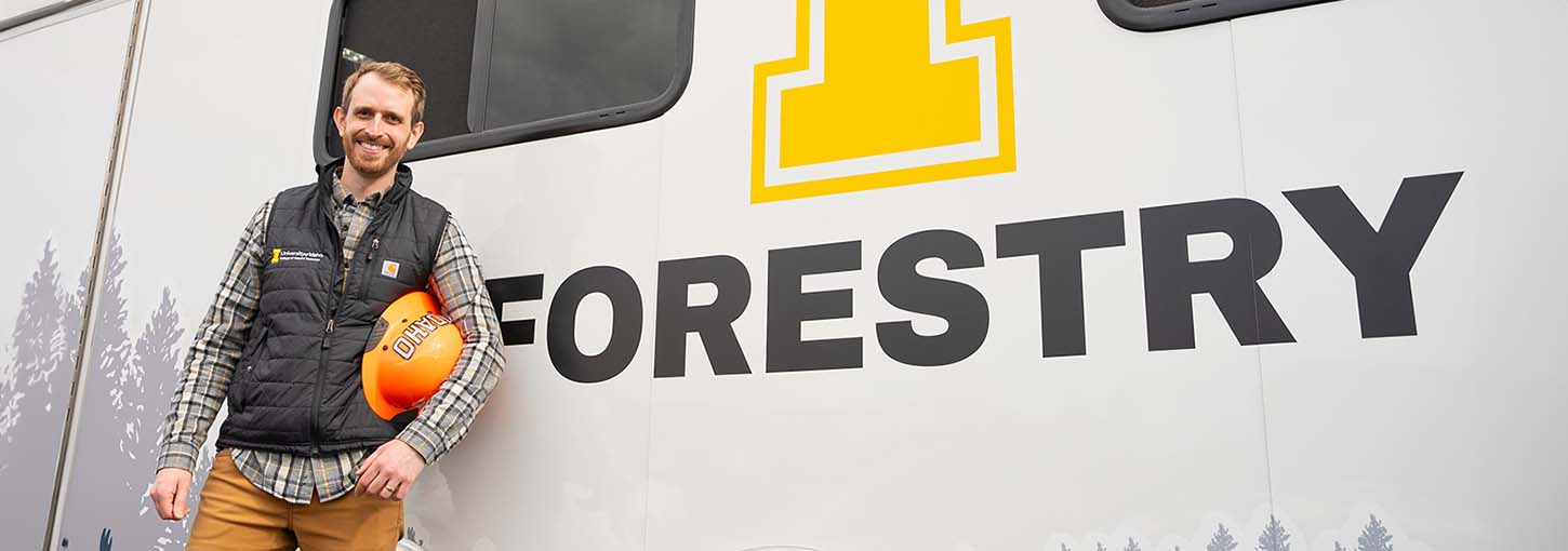 Man holding hard hat stands in front of an enclosed trailer.