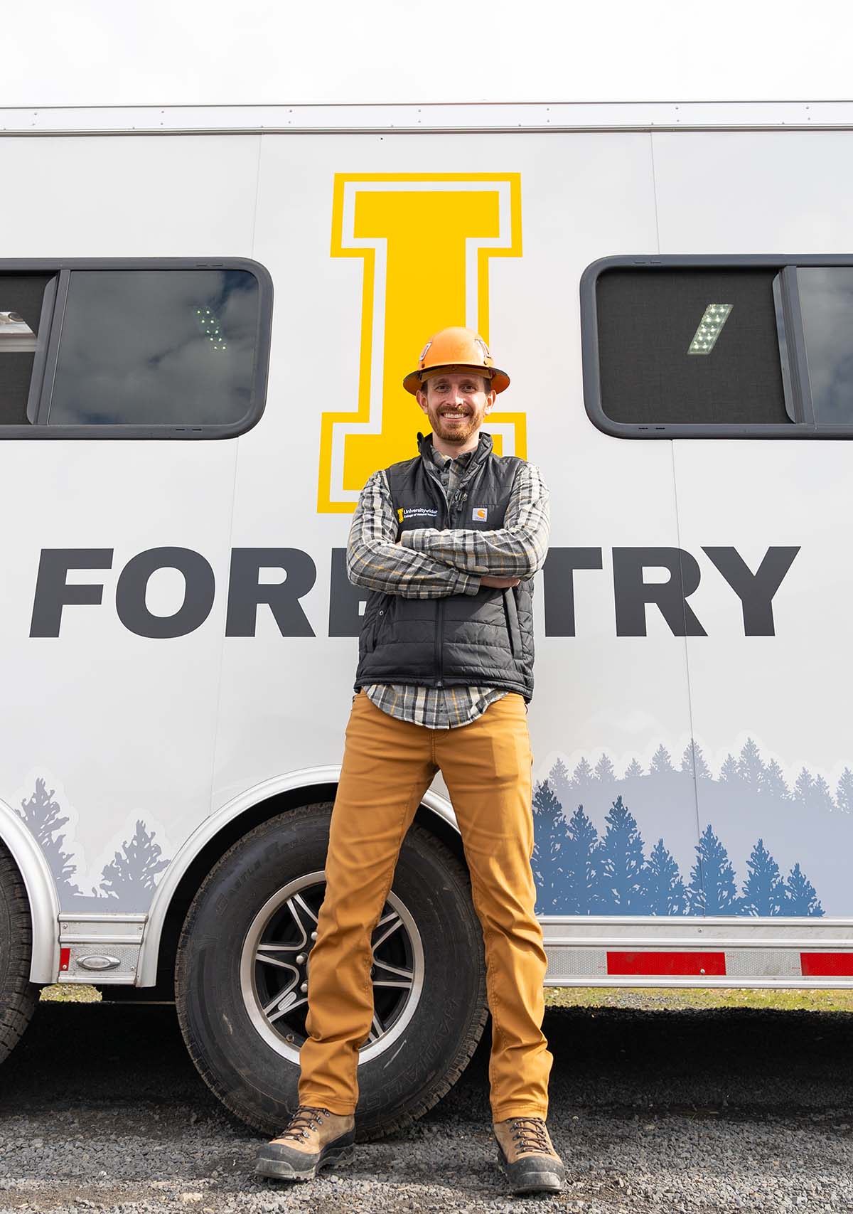 Smiling man stands in front of an enclosed forestry trailer.