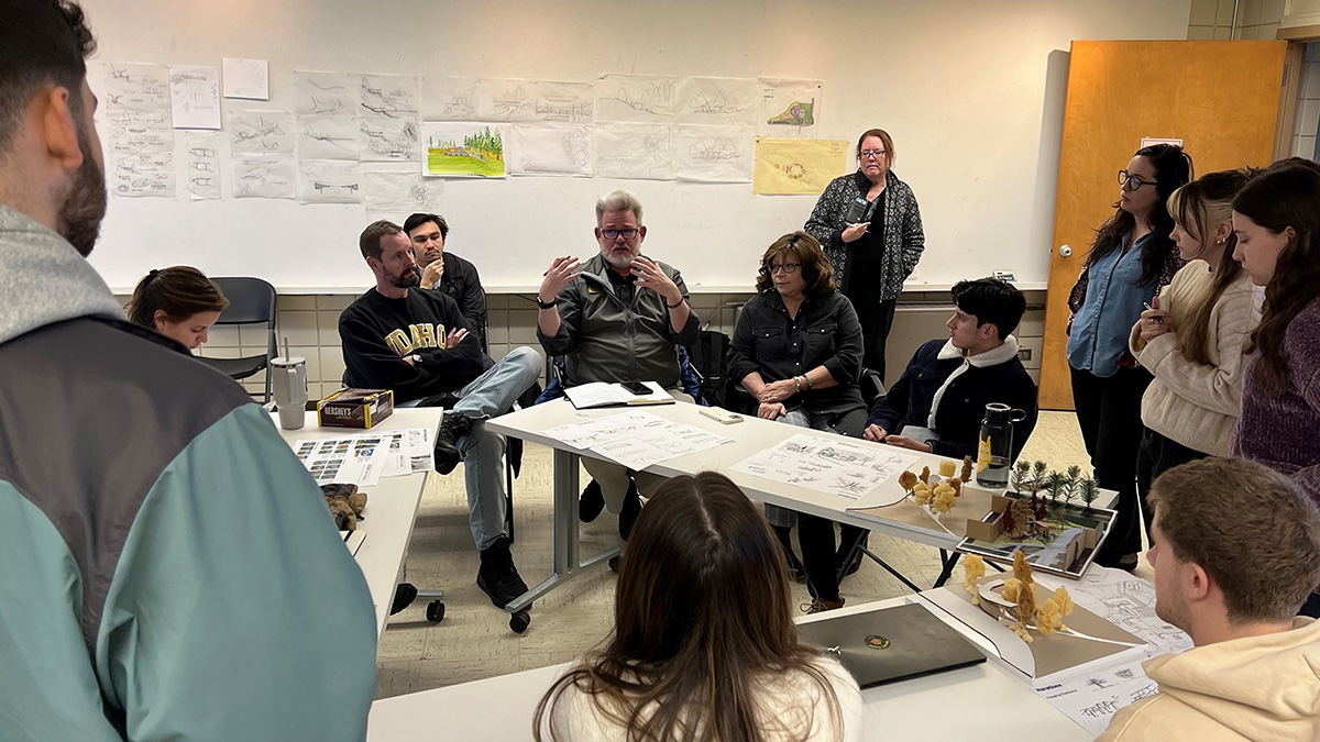 Photo of students and faculty sitting around tables with drawings in the background.