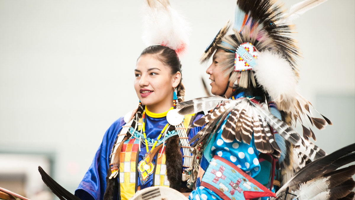 Two Native Americans wearing ceremonial garb.