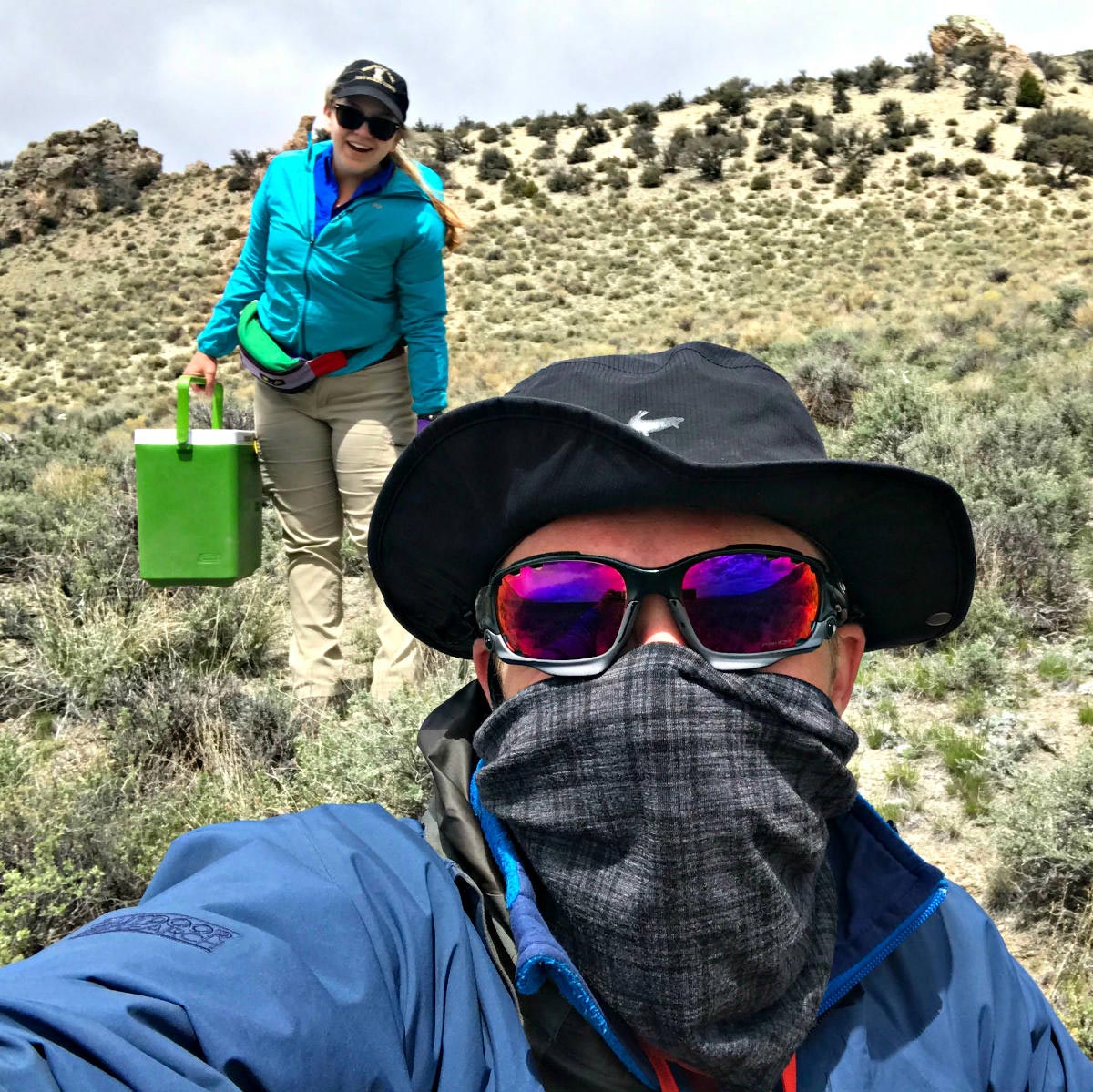 Masked person takes selfie with another person in background