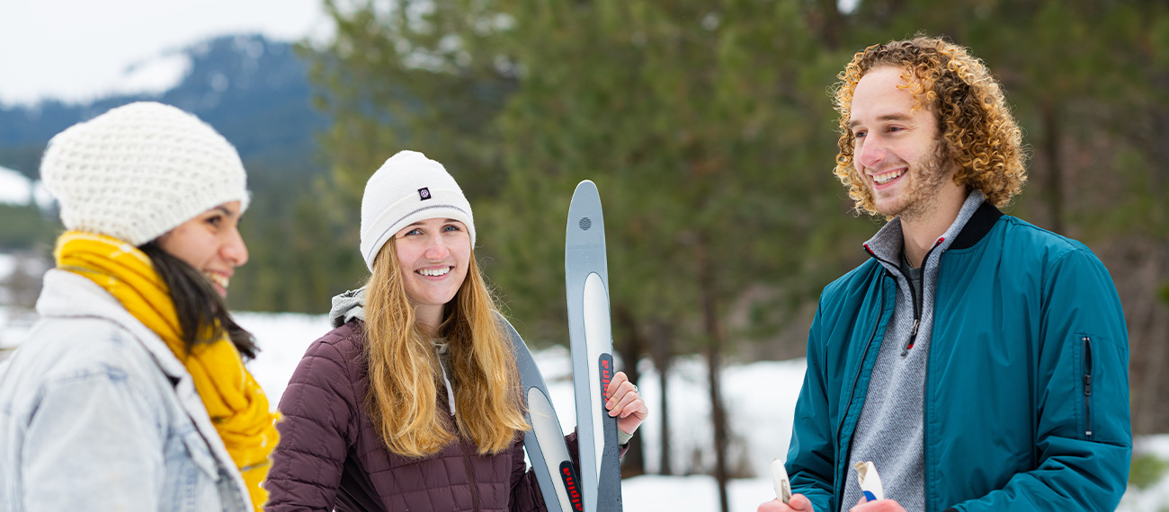 three students standing in a snow covered forest, holding a set of ski's