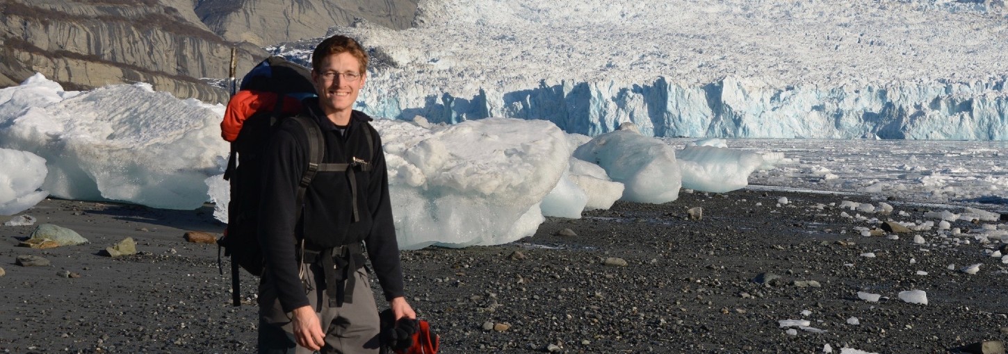 Tim Bartholomaus wears cold weather gear in front of a glacier.