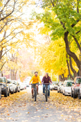 Two students ride down Greek Row in the fall, amid changing leaves.