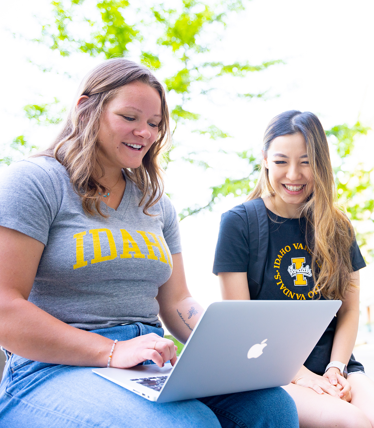 Two girls smiling while looking at a laptop.